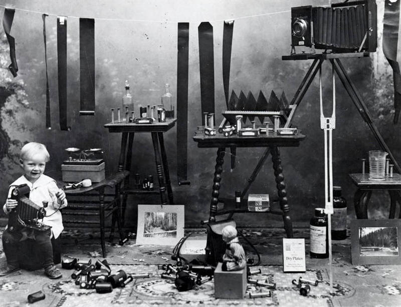 Harold, son of A.M. Whelchel, holding camera. Also shows film, tables, chemicals, etc.