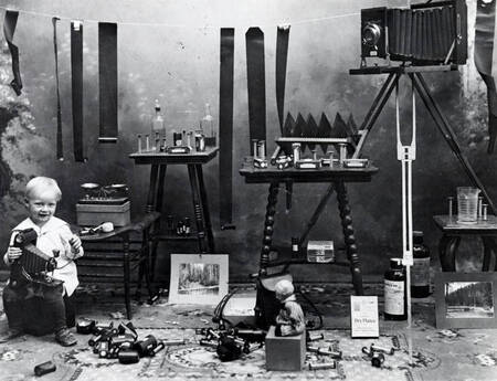 Harold, son of A.M. Whelchel, holding camera. Also shows film, tables, chemicals, etc.
